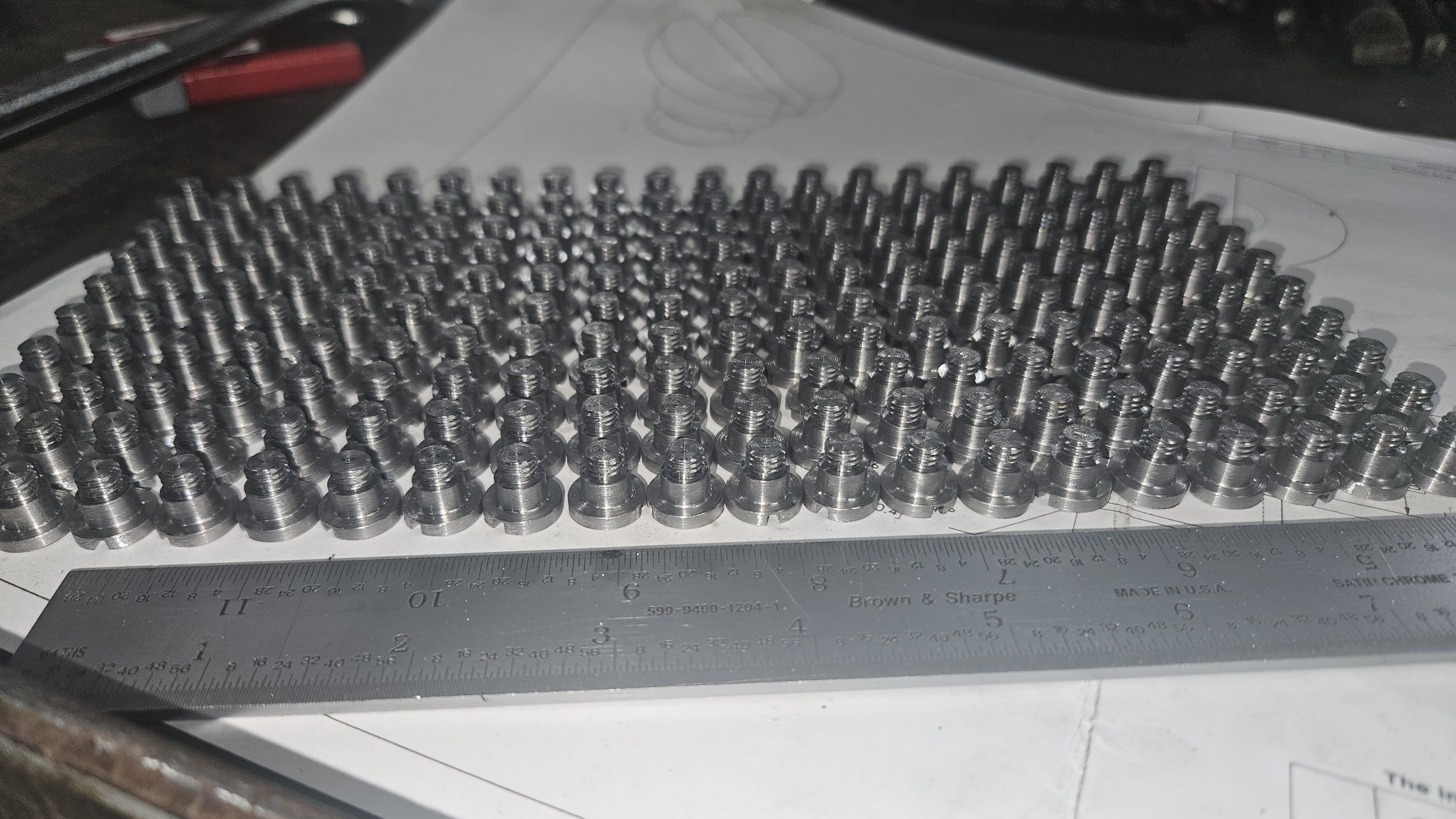 Rows of machined stainless steel shoulder screws laid out on a blueprint