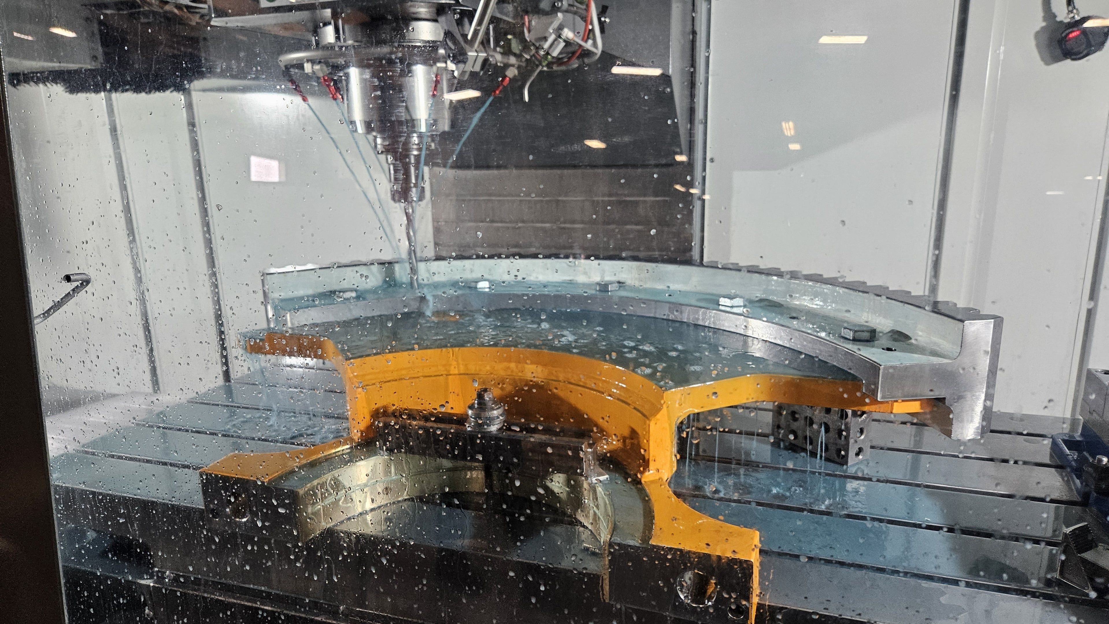 Large curved yellow steel casting being CNC milled with flood coolant