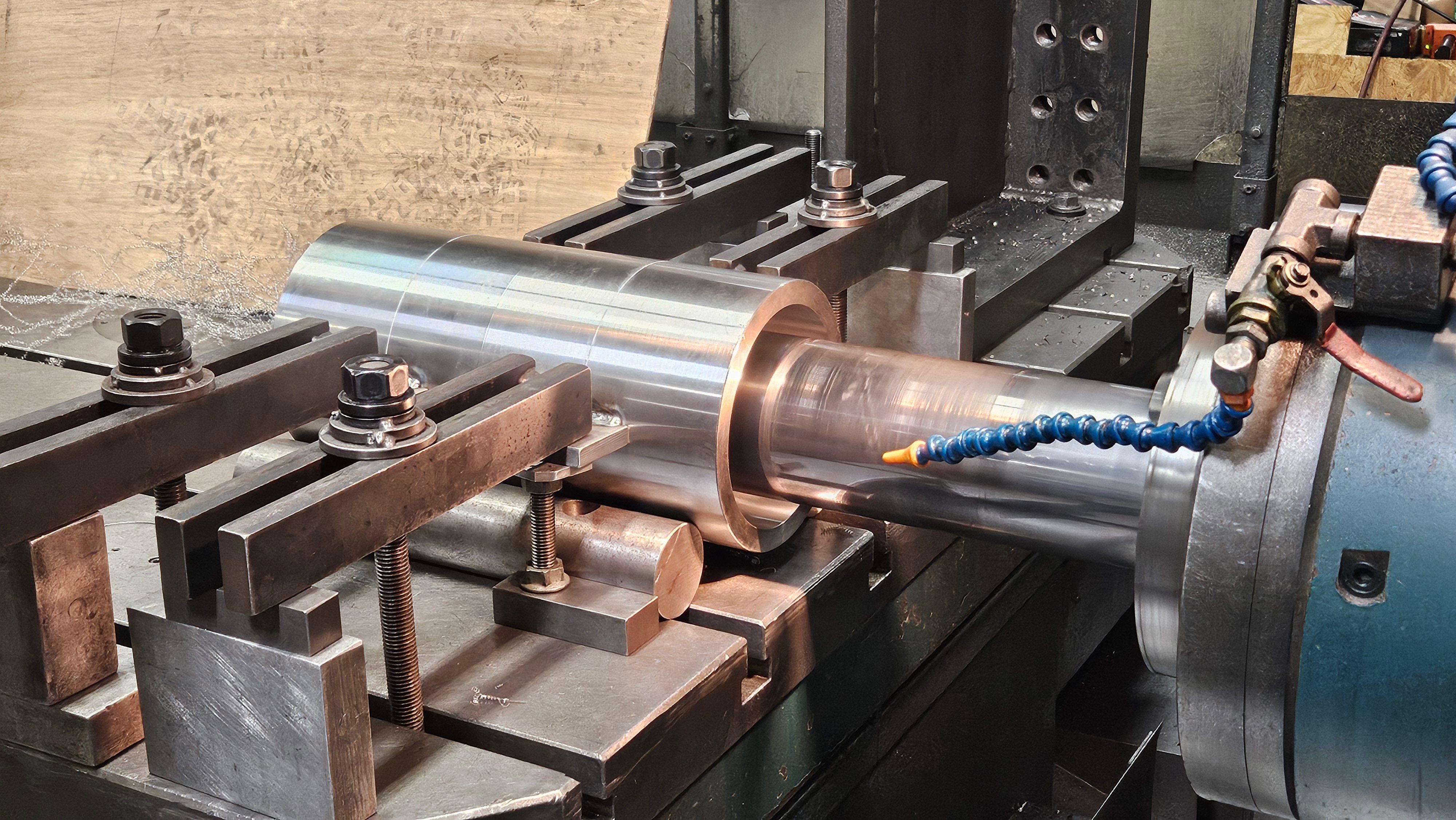 Large polished steel roll being turned and coolant-cooled on a lathe