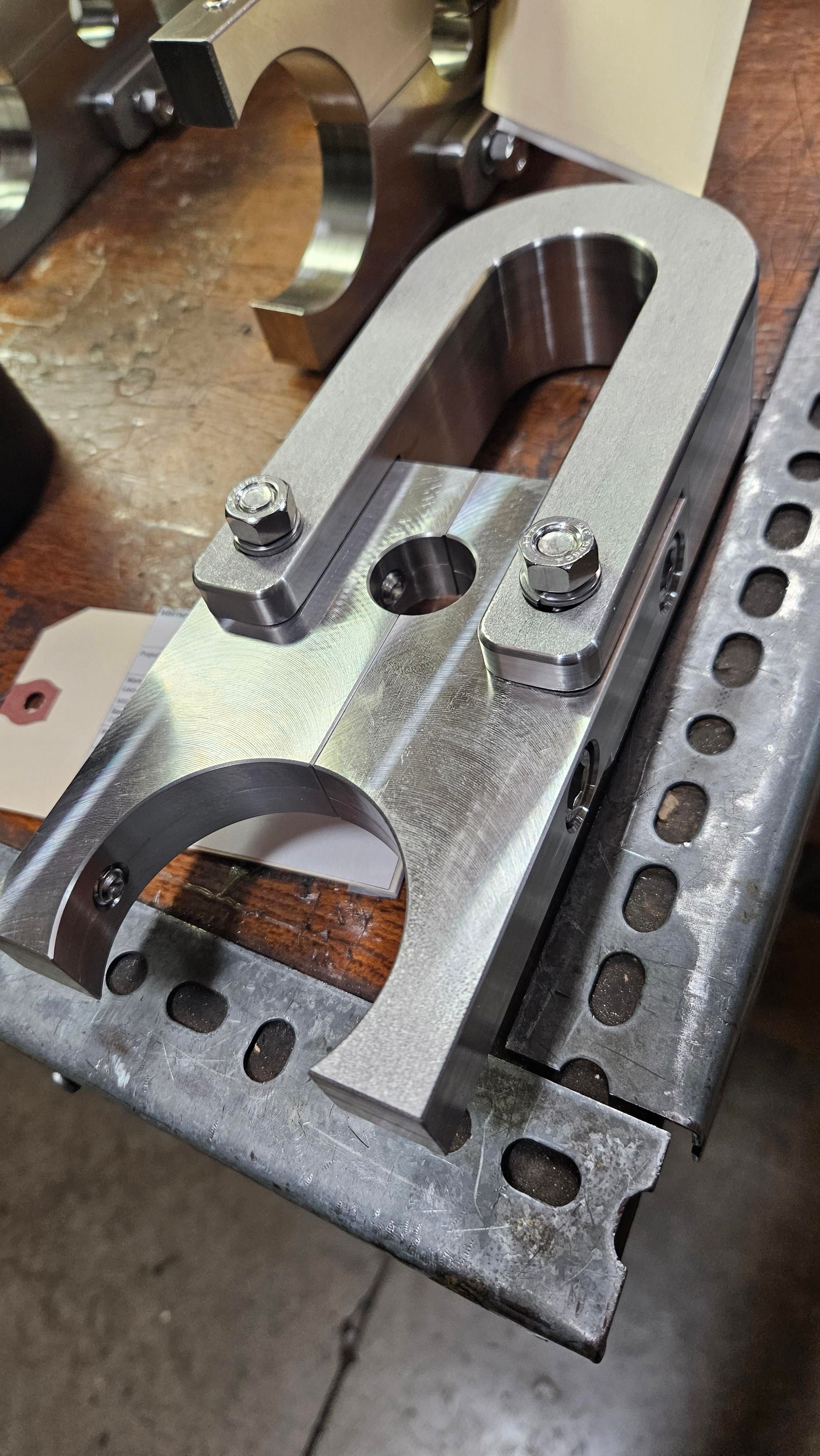 Machined steel yoke bracket with bolted clamps and a bored pivot hole