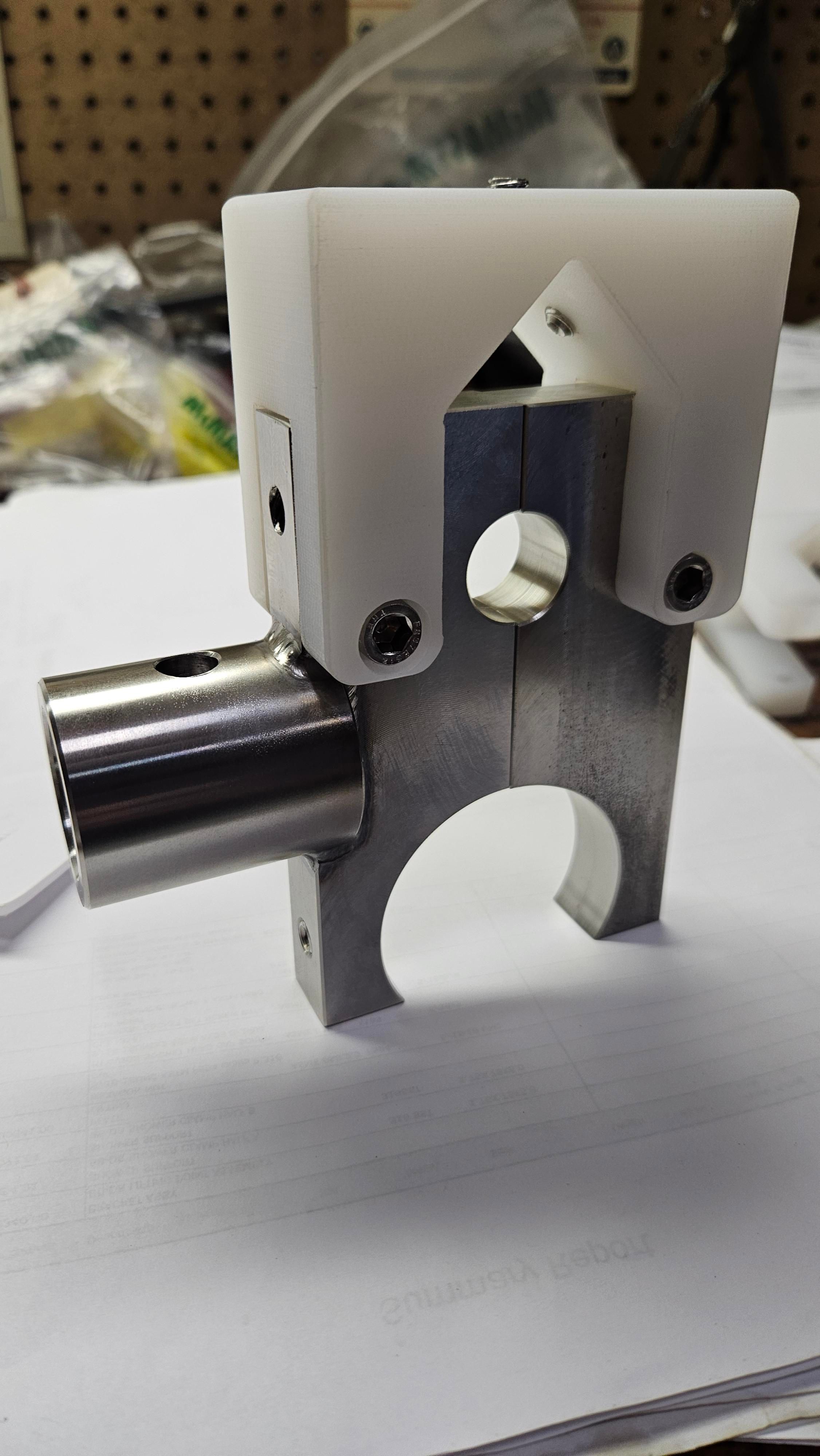 White 3D-printed fixture clamped onto a machined aluminum bracket assembly