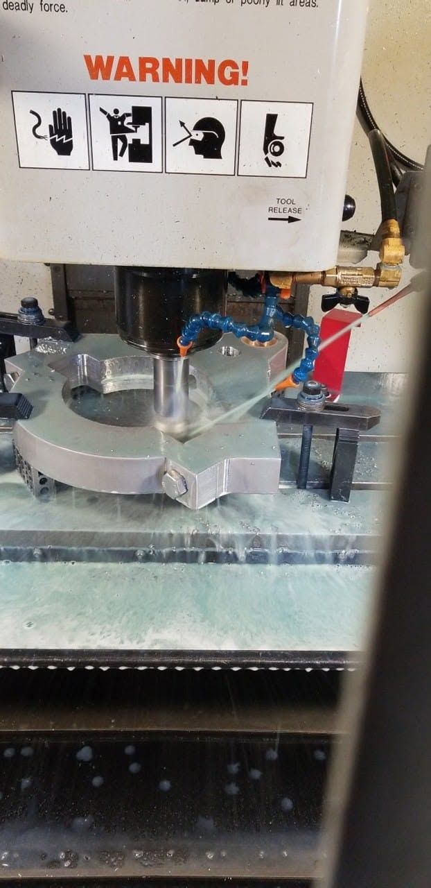 CNC vertical mill boring a star-shaped aluminum part under coolant flow